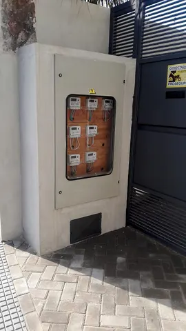 Gabinete exterior de medidores empotrado en un muro, junto al portón de acceso